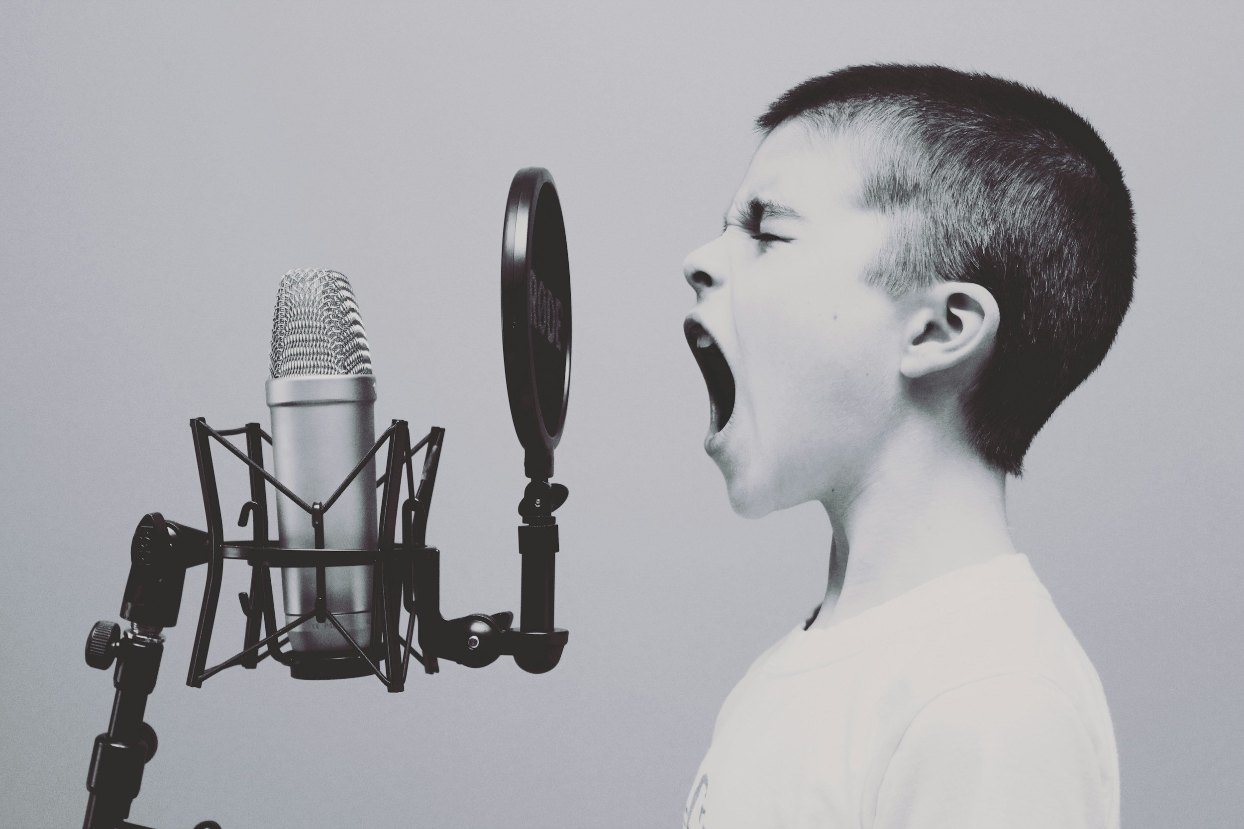 Young boy with short hair singing loudly into a microphone with a pop filter.